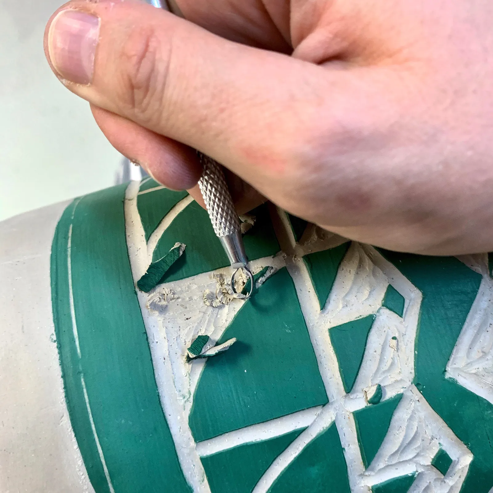 A hand carving a green and white pot