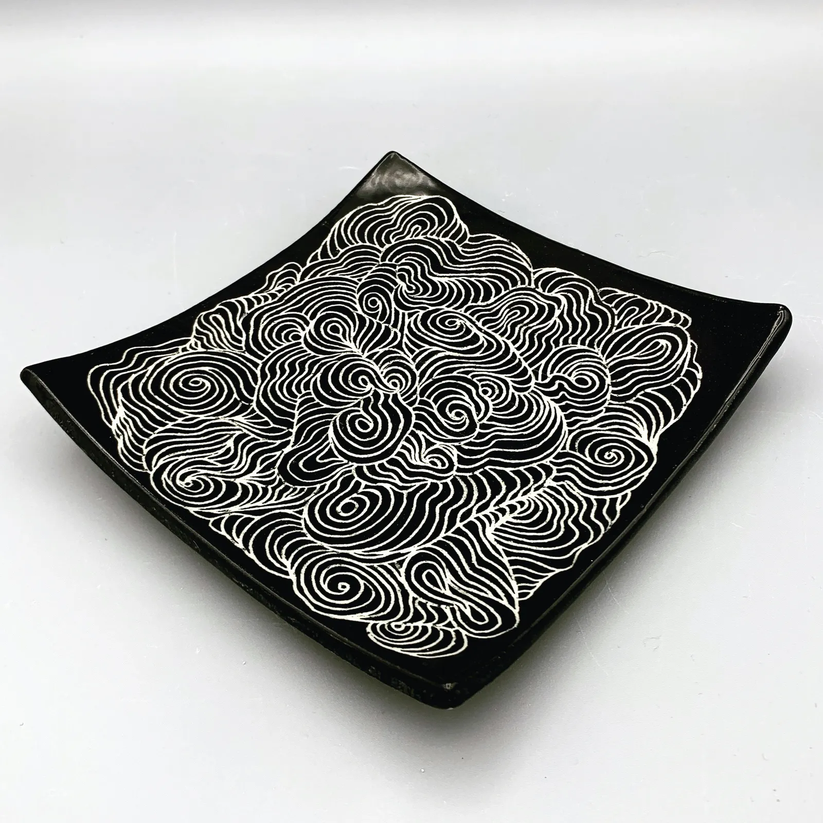 Sgraffito dish, 2021, glazed stoneware fired to Cone 6 oxidation, approx. 1 x 6 x 6 in. A black dish with white carving in a swirling pattern.