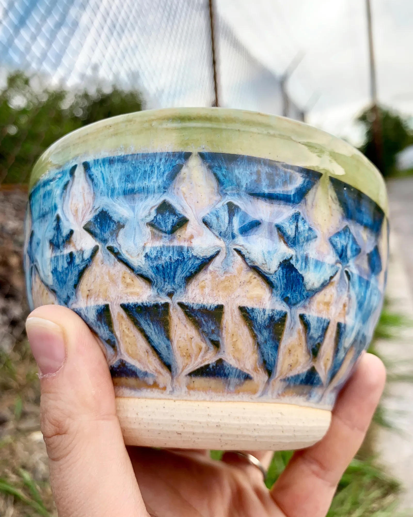 Sgraffito bowl, 2019, glazed stoneware fired to Cone 6 oxidation, approx. 3 x 4 x 4 in. A hand holding a green and honey-colored bowl carved in a geometric pattern.