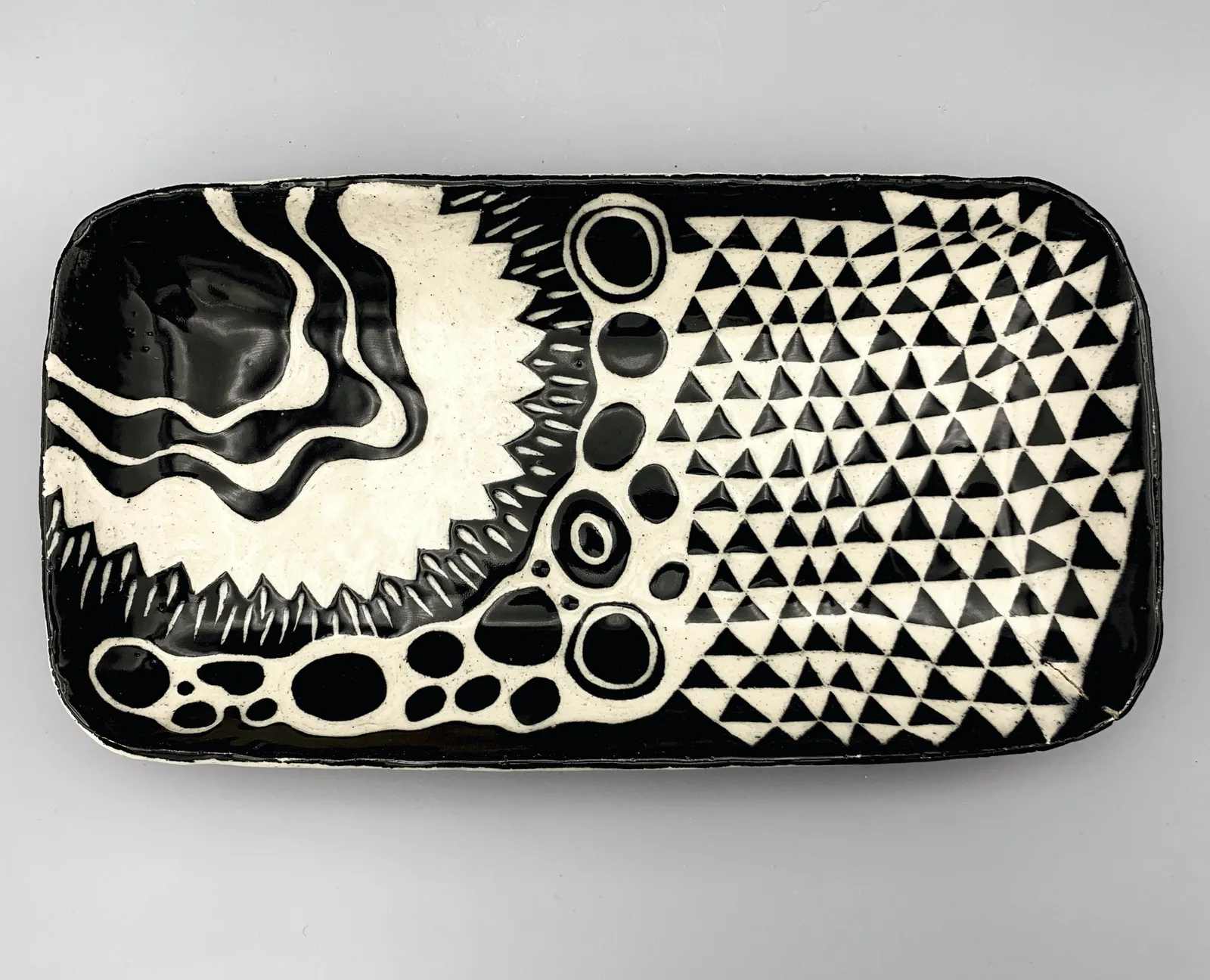 Sgraffito dish, 2021, glazed stoneware fired to Cone 6 oxidation, approx. 1 x 12 x 6 in. A black rectangular dish with white carving in a variety of patterns.