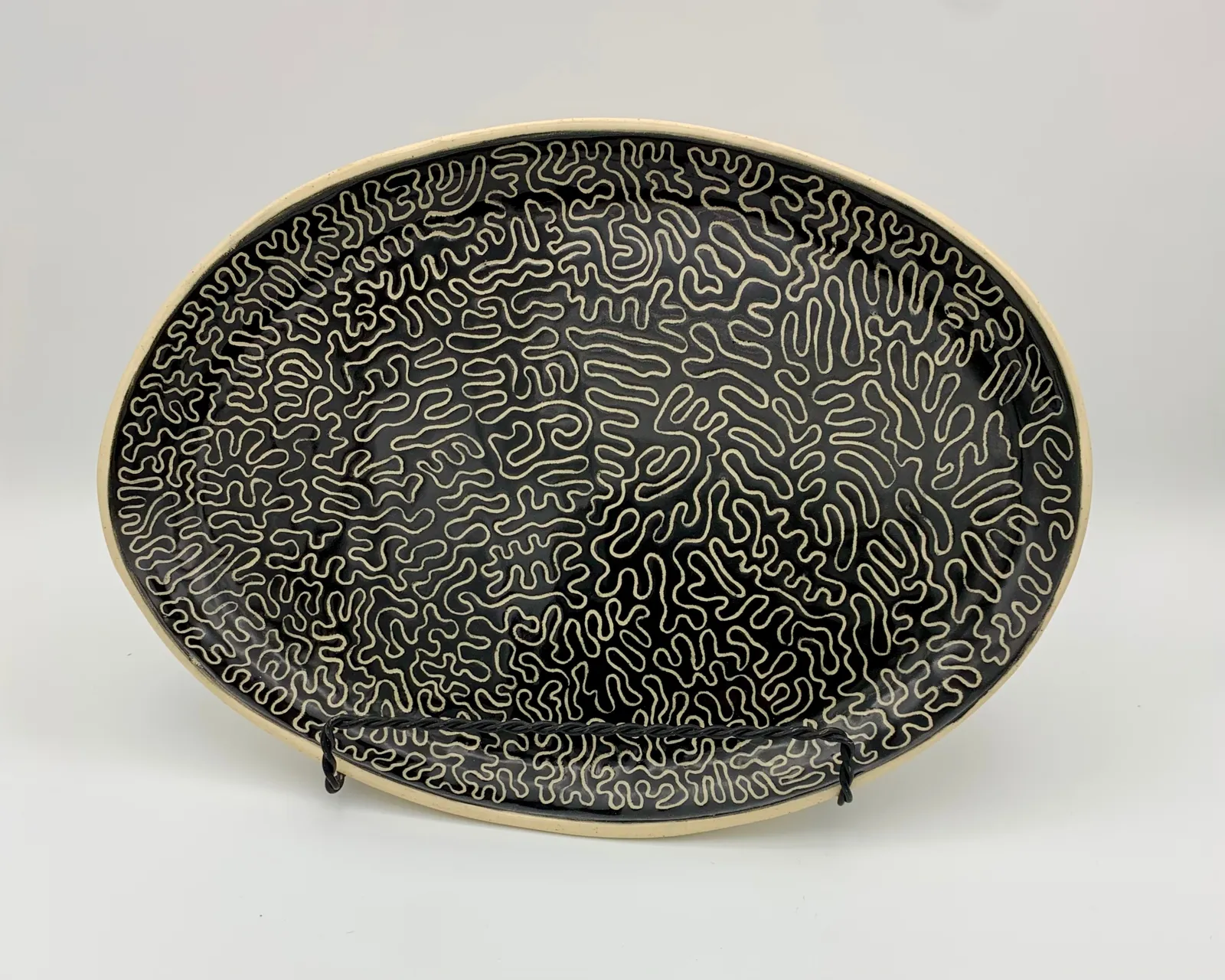 Sgraffito dish, 2024, glazed stoneware fired to Cone 6 oxidation, approx. 1 x 10 x 7 in. A black dish with white carving in a linear pattern.