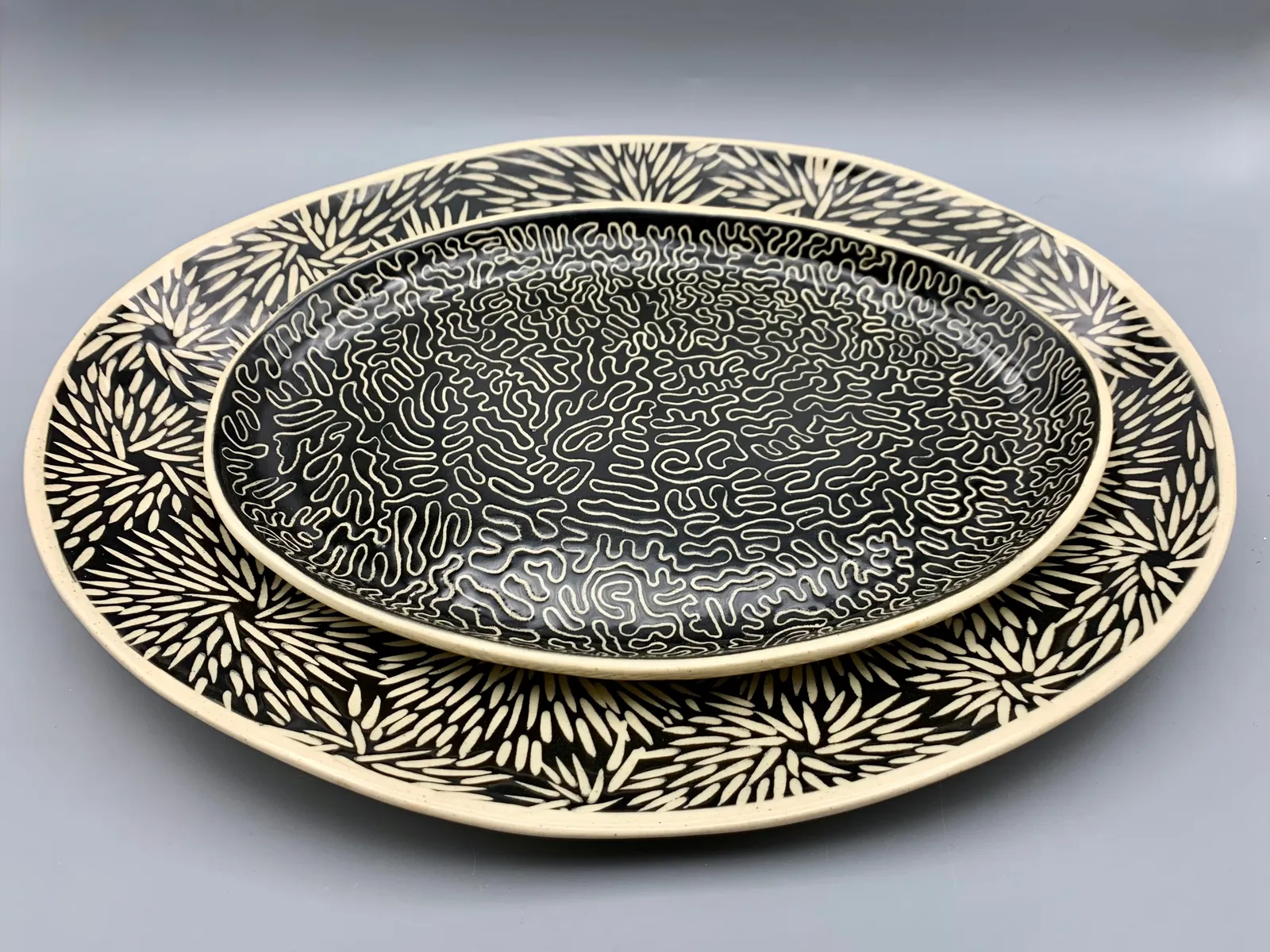 Sgraffito dishes, 2024, glazed stoneware fired to Cone 6 oxidation, x x in. A stack of two black and white dishes carved in different patterns.