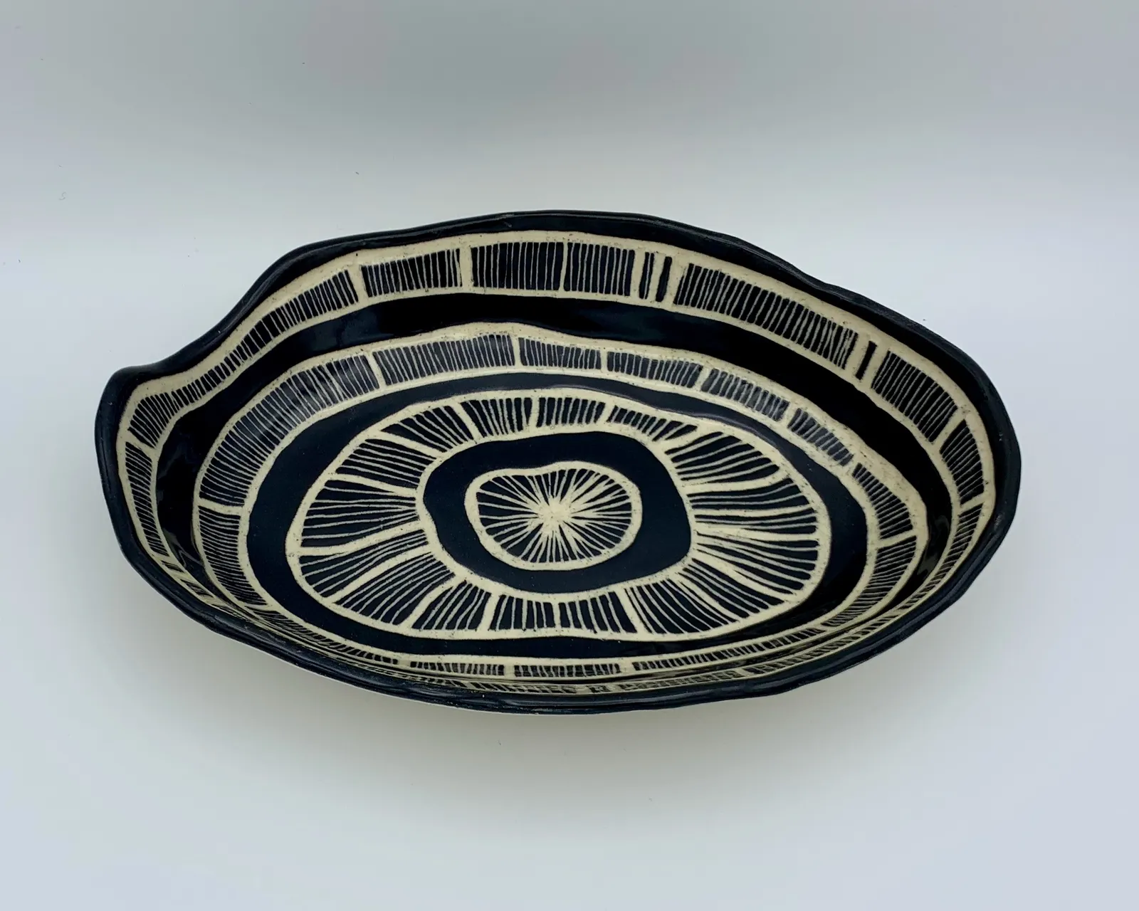 Sgraffito dish, 2019, glazed stoneware fired to Cone 6 oxidation, approx. 2 x 10 x 7 in. A black dish with white carving in a linear pattern.