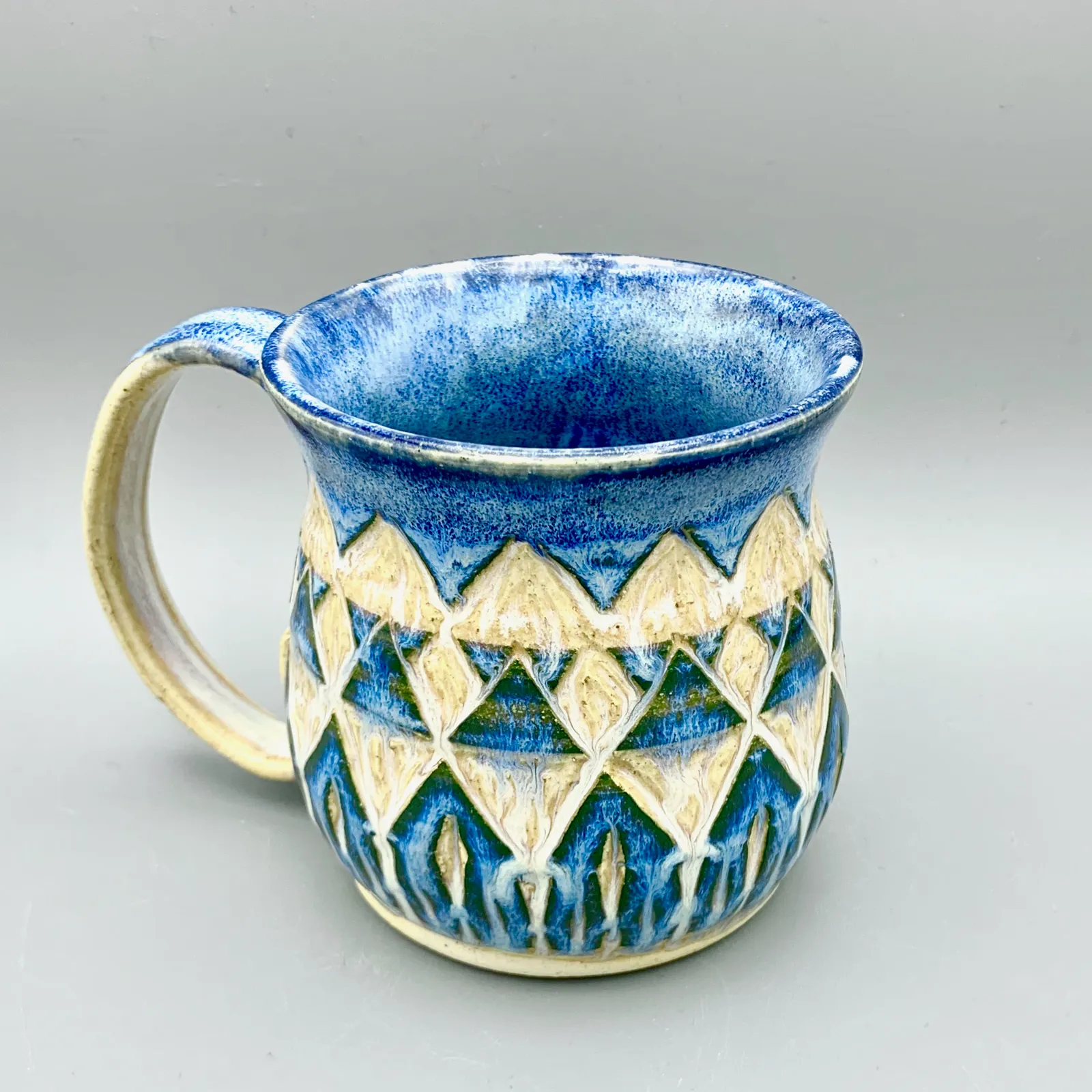 Sgraffito mug, 2019, glazed stoneware fired to Cone 6 oxidation, 4 x 6 x 4 in. A blue, green, and honey-colored mug carved in a geometric pattern.