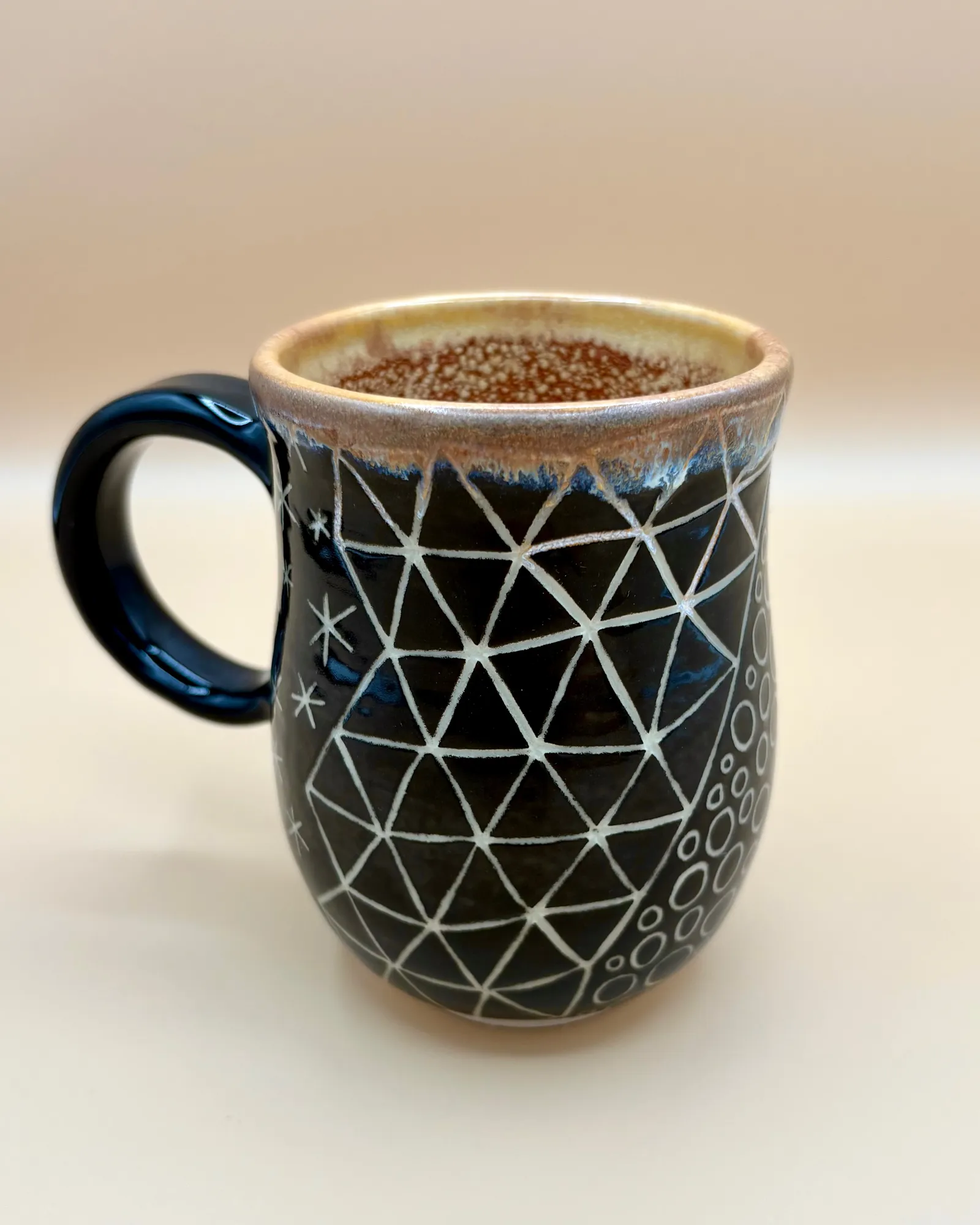 Sgraffito mug, 2026, glazed stoneware fired to Cone 6 oxidation, approx. 4 x 5 x 4 in. A black mug with white carving in a variety of patterns.