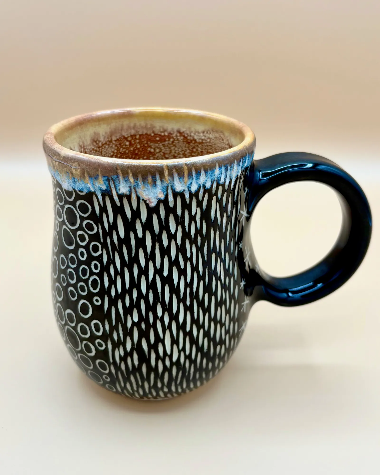 Sgraffito mug, 2026, glazed stoneware fired to Cone 6 oxidation, 4.5 x 5.5 x 3.5 in. A black mug with white carving in a variety of patterns.