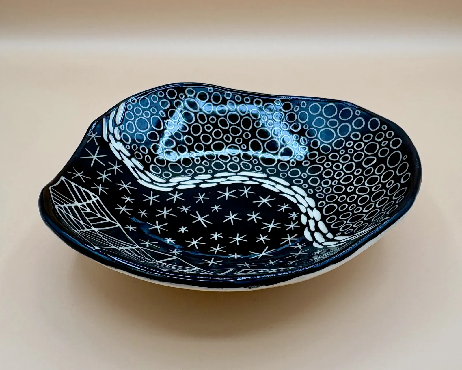 Sgraffito dish, 2026, glazed stoneware fired to Cone 6 oxidation, 2 x 7 x 7 in. A black dish with white carving in a variety of patterns.