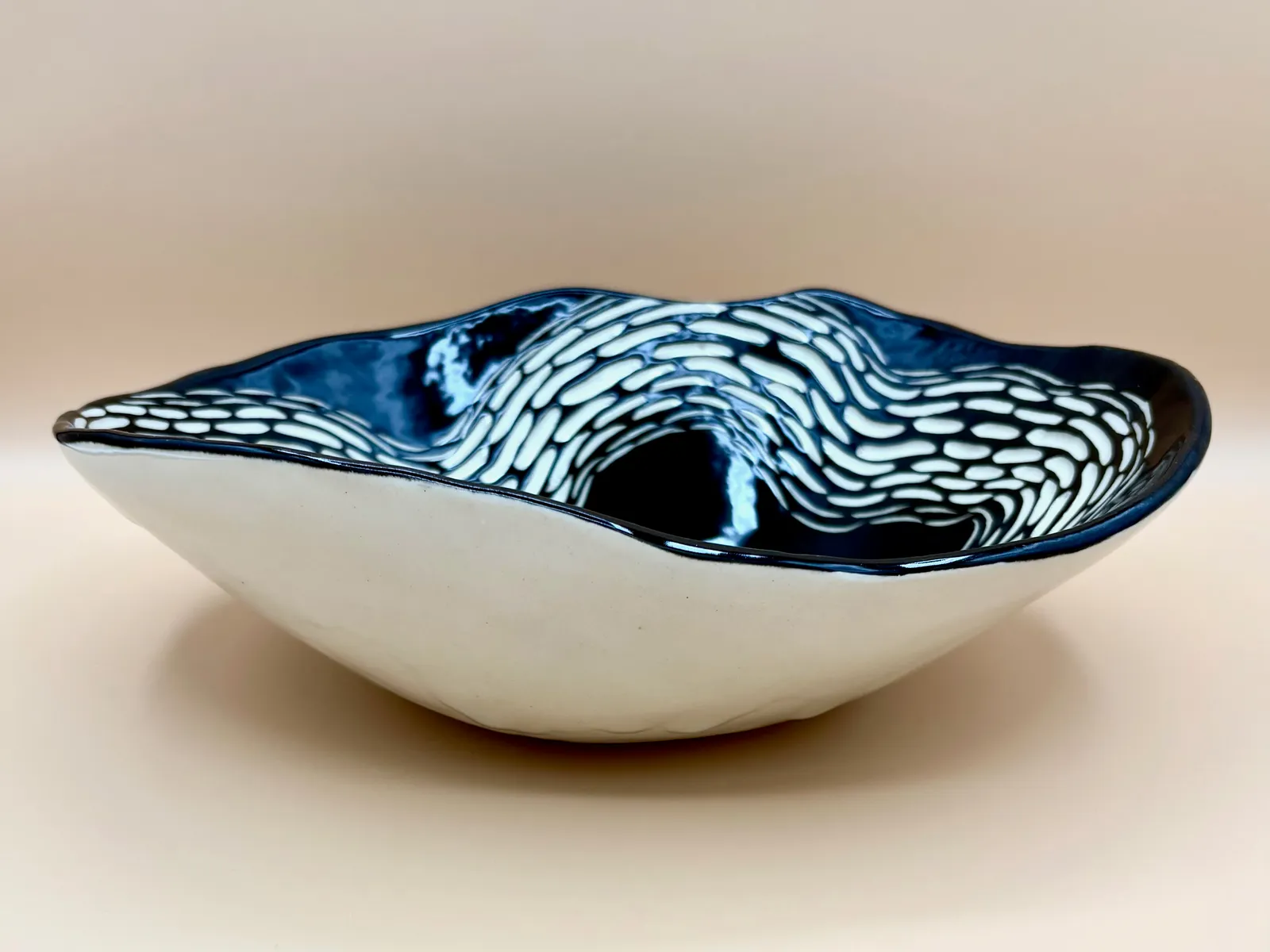 Sgraffito dish, 2026, glazed stoneware fired to Cone 6 oxidation, 3.5 x 11 x 9 in. A black dish with white carving in a wavy pattern.