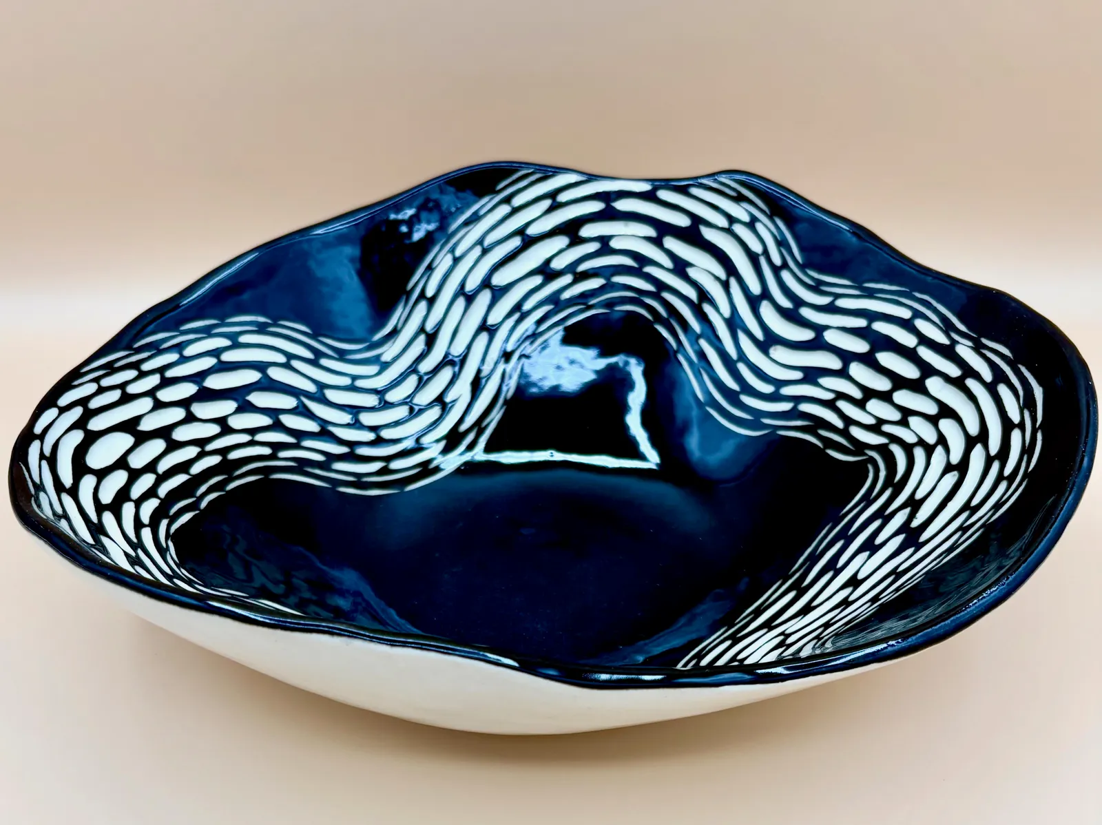Sgraffito dish, 2026, glazed stoneware fired to Cone 6 oxidation, 3.5 x 11 x 9 in. A black dish with white carving in a wavy pattern.