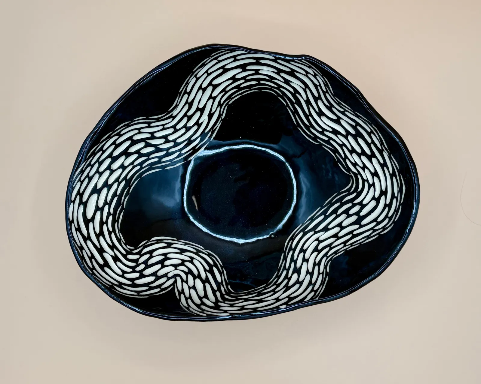 Sgraffito dish, 2026, glazed stoneware fired to Cone 6 oxidation, 3.5 x 11 x 9 in. A black dish with white carving in a wavy pattern.