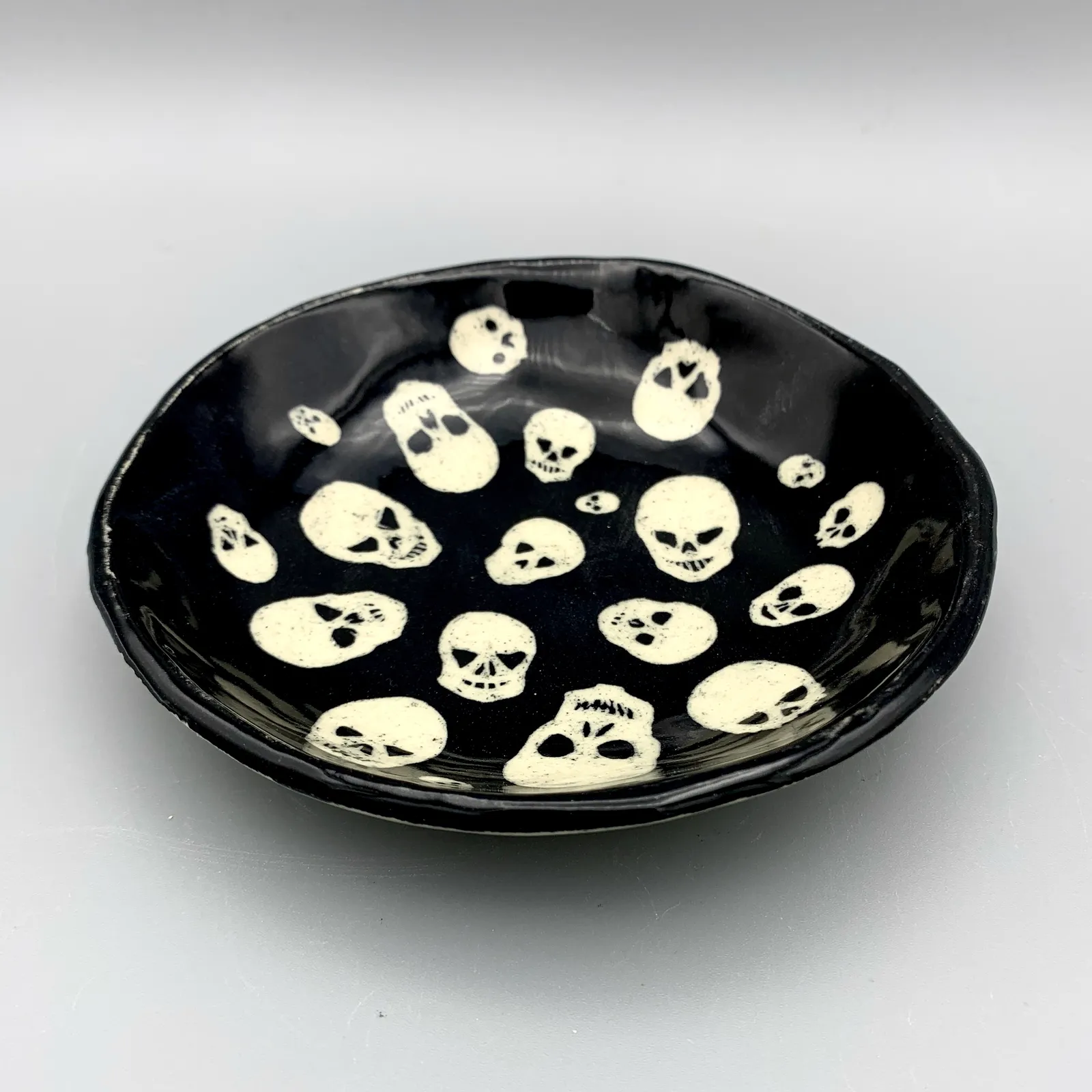 Sgraffito skull dish, 2021, glazed stoneware fired to Cone 6 oxidation, approx. 1 x 6 x 6 in. A black dish with white carving in a skull pattern.