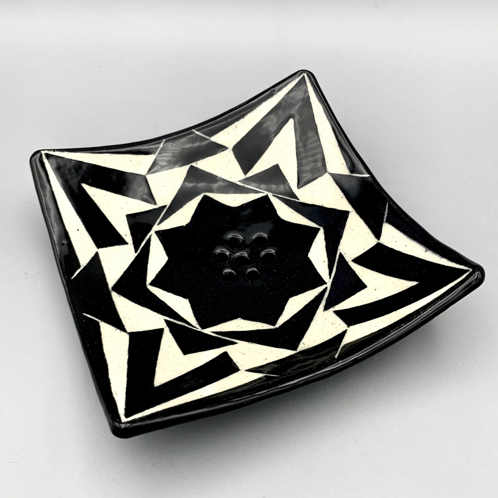 Sgraffito soap dish, 2021, glazed stoneware fired to Cone 6 oxidation, approx. 1 x 6 x 6 in. A black and white soap dish carved in a geometric pattern.