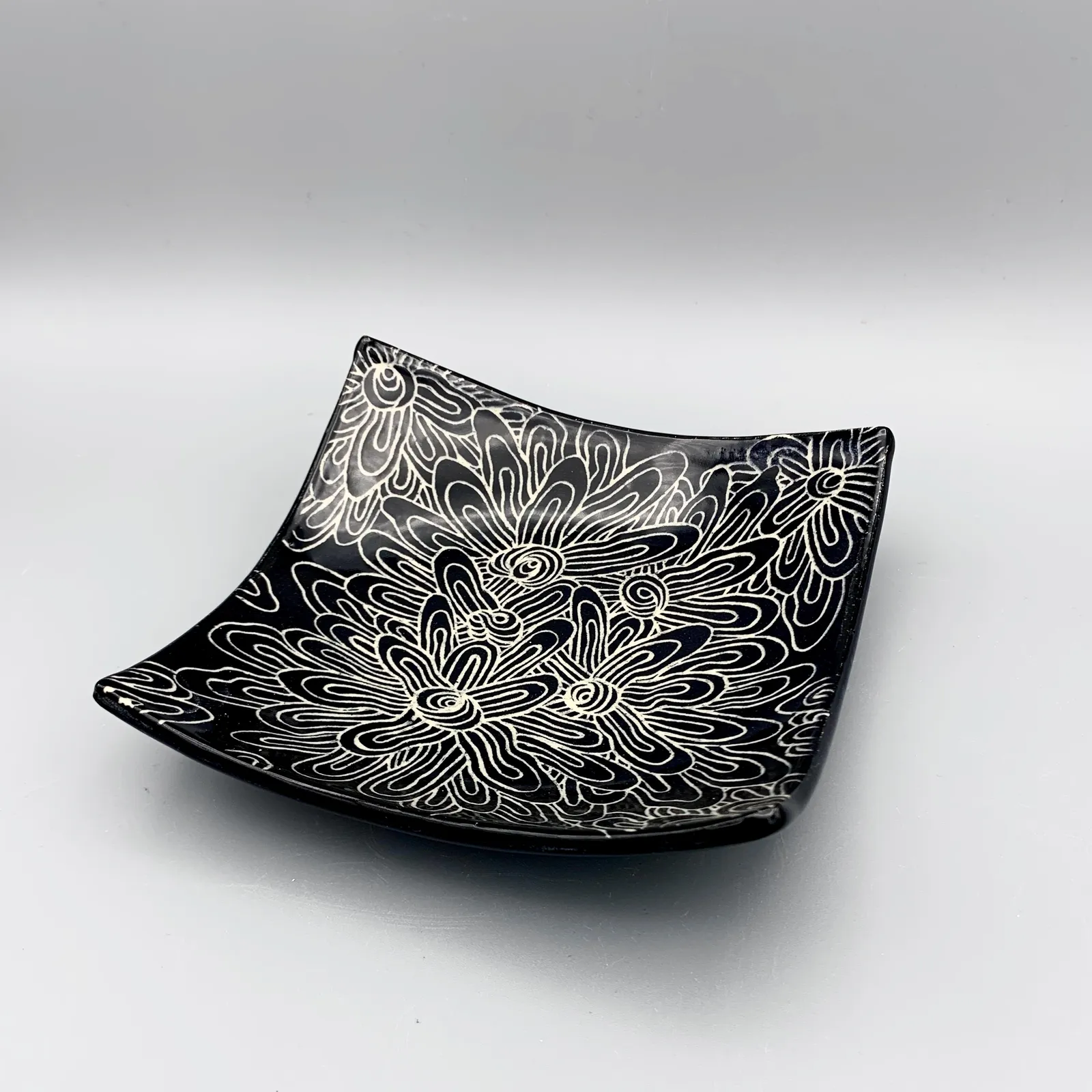 Sgraffito dish, 2021, glazed stoneware fired to Cone 6 oxidation, approx. 1 x 6 x 6 in. A black dish with white carving in an abstract floral pattern.