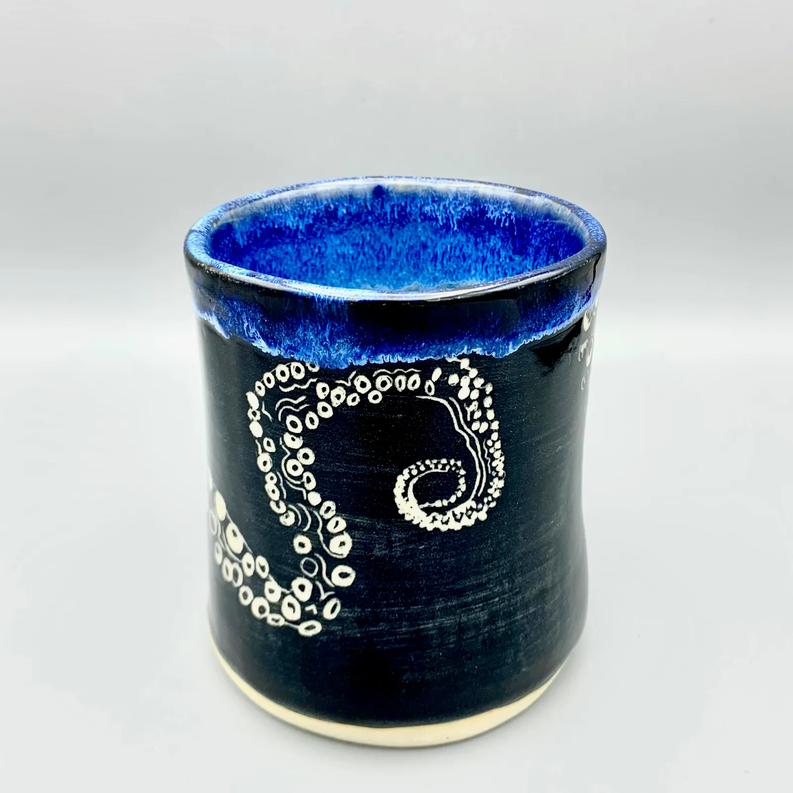 Sgraffito octopus tumbler, 2021, glazed stoneware fired to Cone 6 oxidation, 5 x 4 x 4 in. A black tumbler with white carving of an octopus tentacle.
