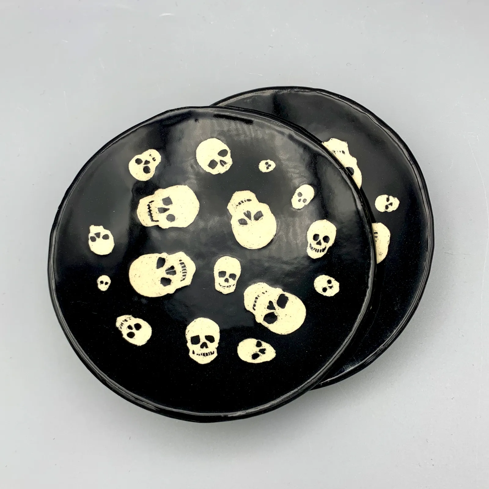 Sgraffito skull dish, 2021, glazed stoneware fired to Cone 6 oxidation, approx. 1 x 6 x 6 in. A black dish with white carving in a skull pattern.