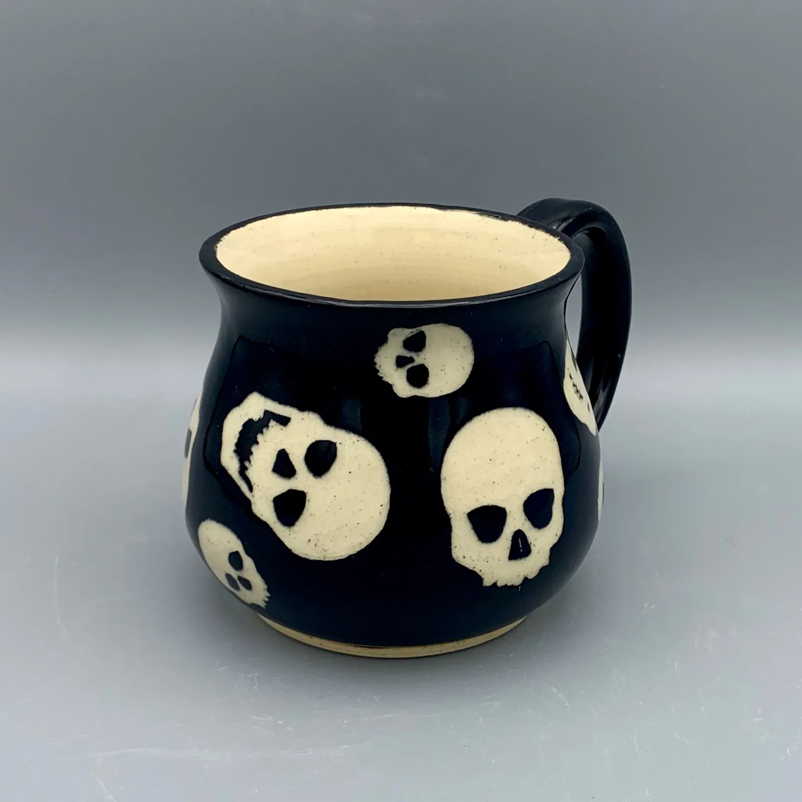 Sgraffito mug, 2021, glazed stoneware fired to Cone 6 oxidation, approx. 4 x 5 x 4 in. A black mug with white carving in a skull pattern.