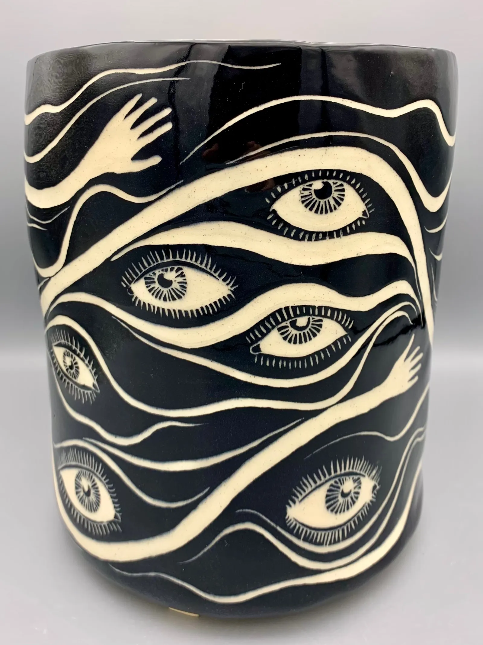 Hand-built sgraffito planter, 2021, glazed stoneware fired to Cone 6 oxidation, 9 x 8 x 8 in. A black and white planter carved in a pattern of eyes and hands.