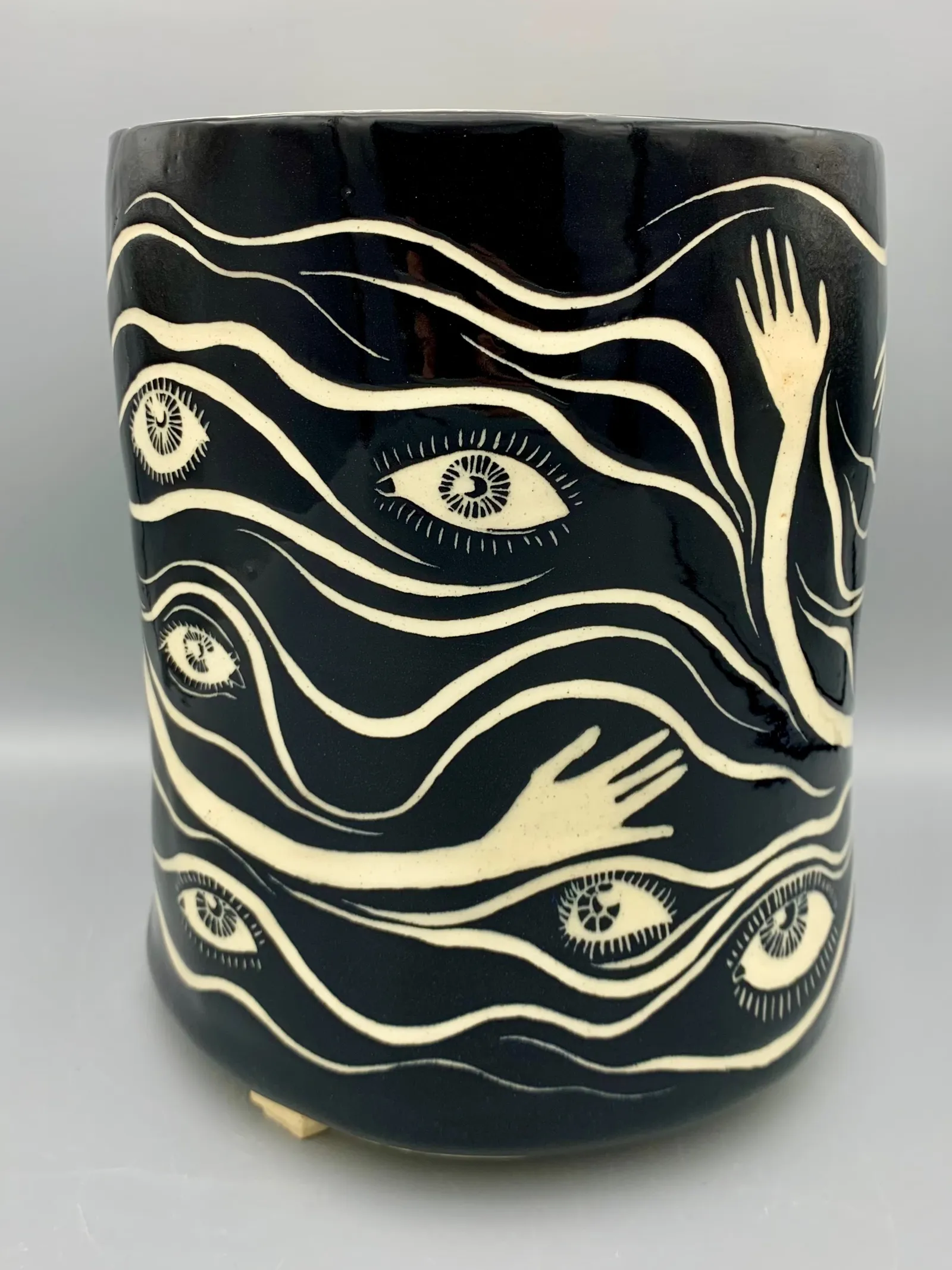 Hand-built sgraffito planter, 2021, glazed stoneware fired to Cone 6 oxidation, 9 x 8 x 8 in. A black and white planter carved in a pattern of eyes and hands.