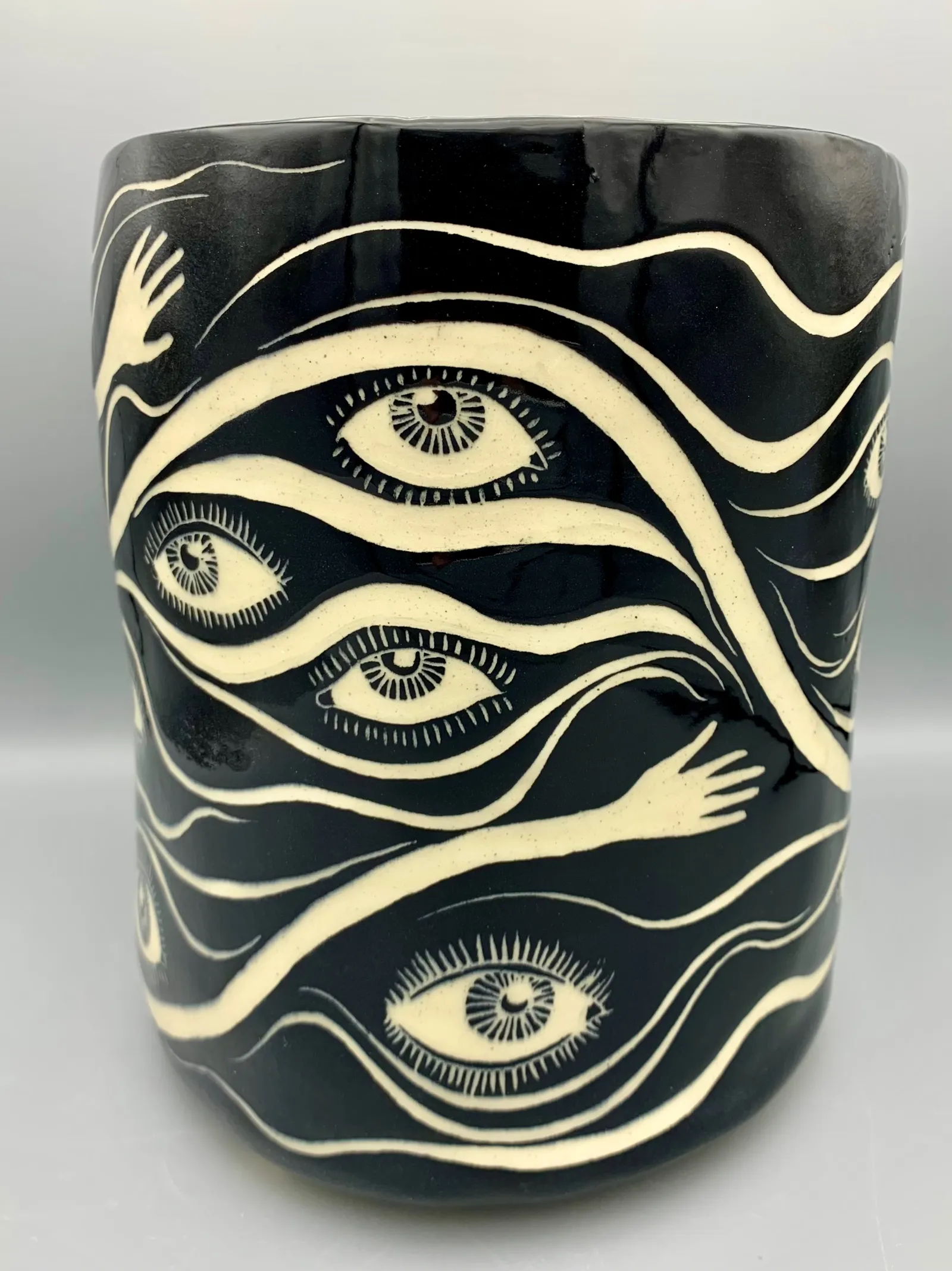 Hand-built sgraffito planter, 2021, glazed stoneware fired to Cone 6 oxidation, 9 x 8 x 8 in. A black and white planter carved in a pattern of eyes and hands.