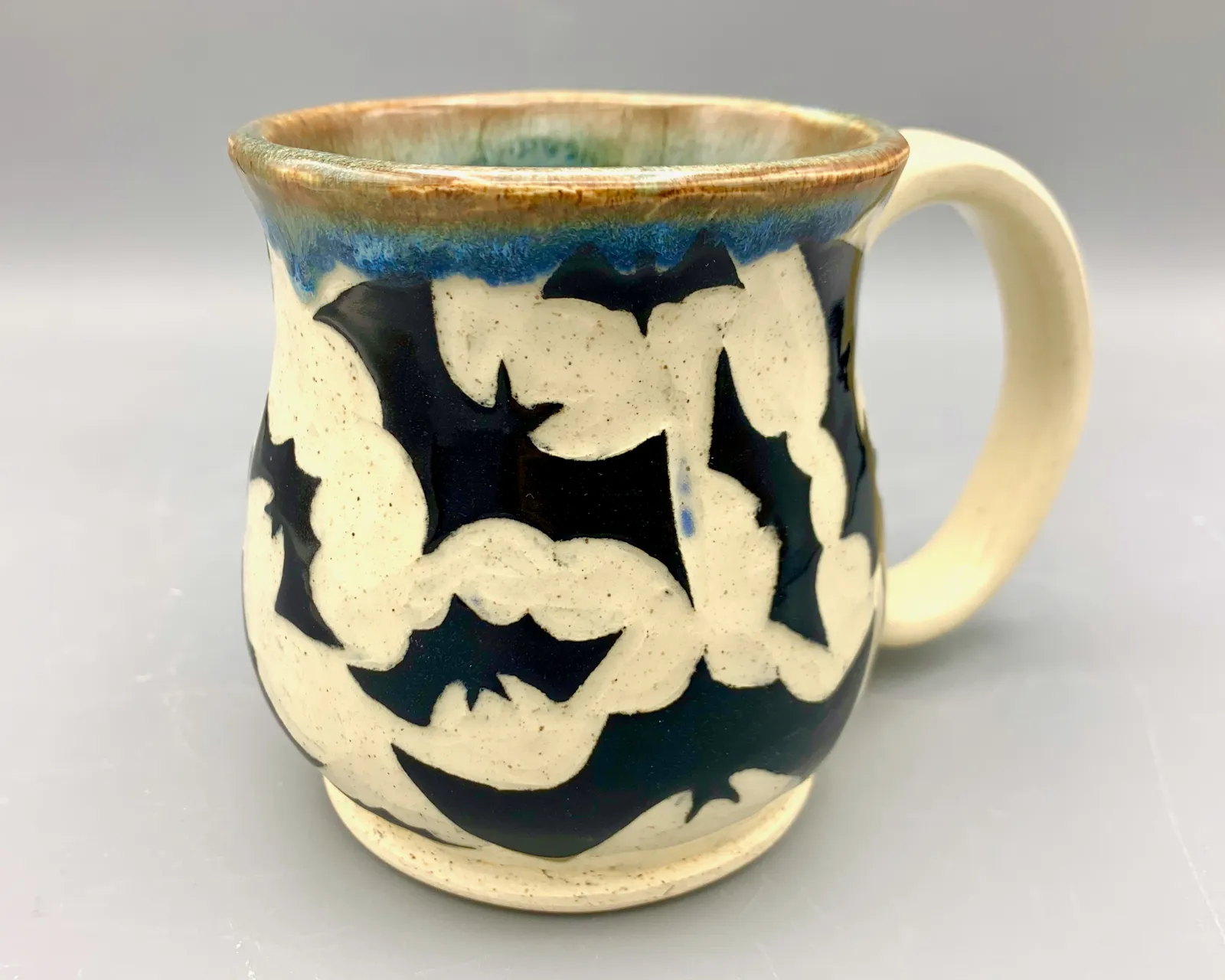Sgraffito mug, 2023, glazed stoneware fired to Cone 6 oxidation, approx. 4 x 5 x 4 in. A black and white mug carved in a bat pattern.