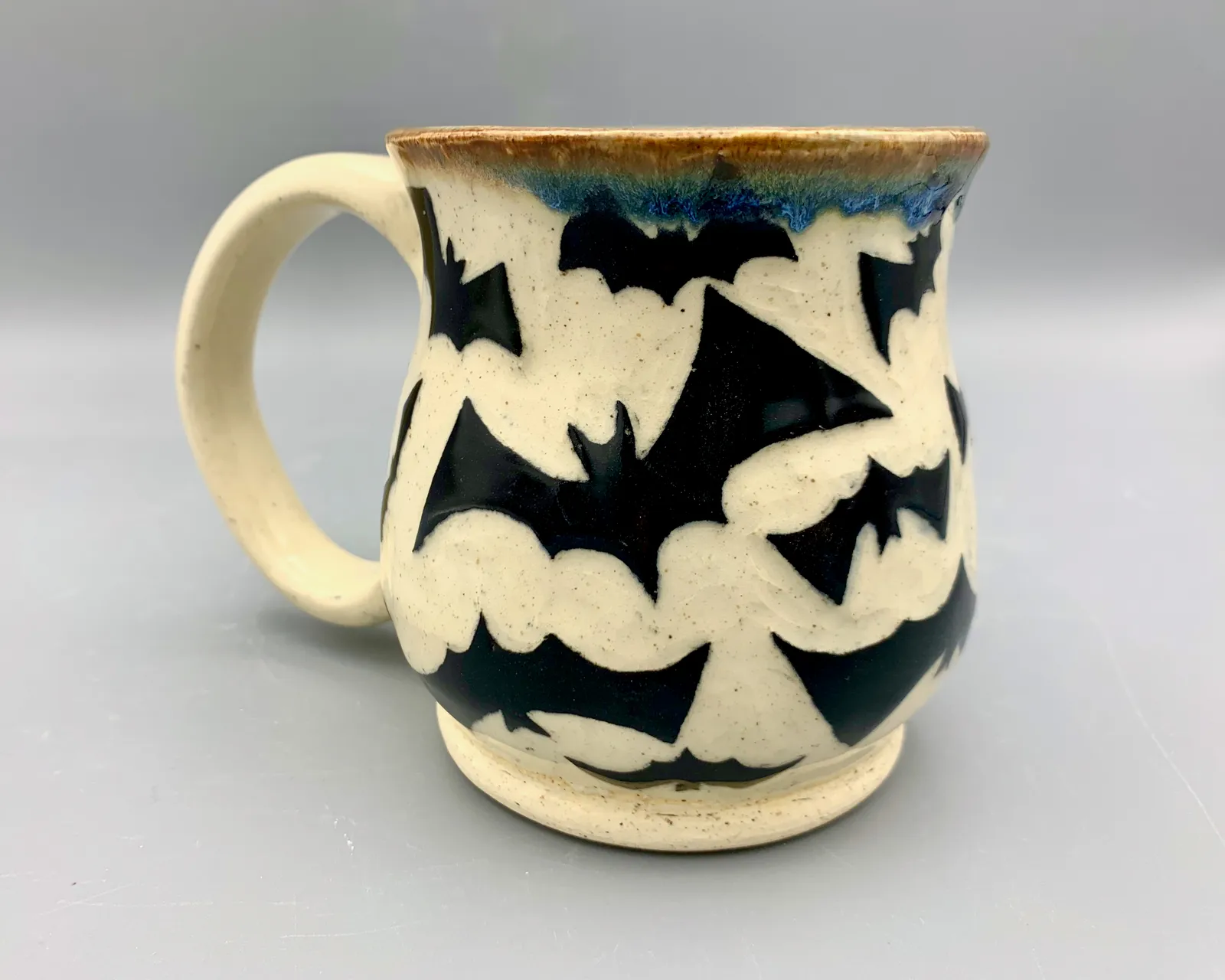 Sgraffito mug, 2023, glazed stoneware fired to Cone 6 oxidation, approx. 4 x 5 x 4 in. A black and white mug carved in a bat pattern.