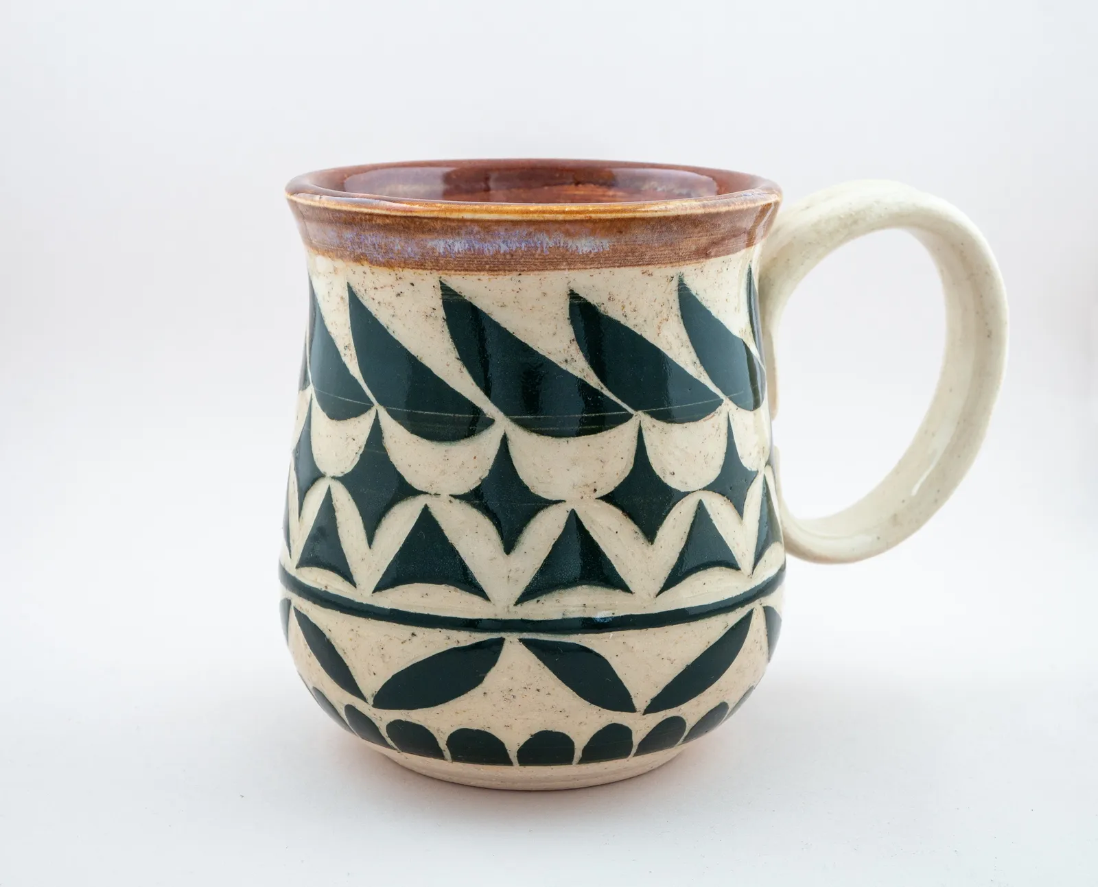 Sgraffito mug, 2019, glazed stoneware fired to Cone 6 oxidation, 4 x 5 x 4 in. A dark green and white mug carved in a geometric pattern.