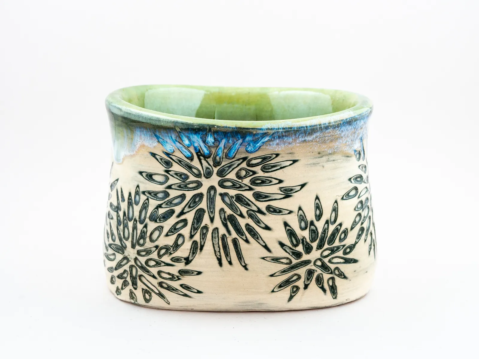 Sgraffito cup, 2019, glazed stoneware fired to Cone 6 oxidation, approx. 3 x 4 x 3 in. A white cup with green and white carving in a floral pattern.